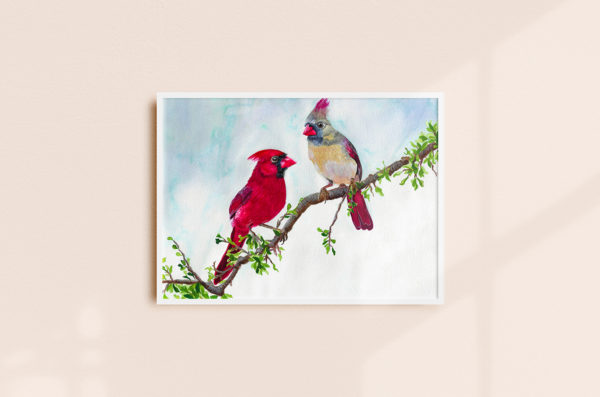 a framed watercolor painting of a male and female cardinal perched on a leafy branch