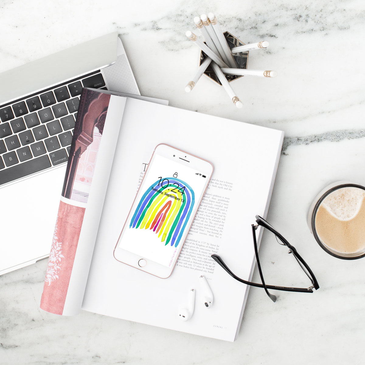 flat lay of laptop, magazine, iphone with rainbow image, glasses