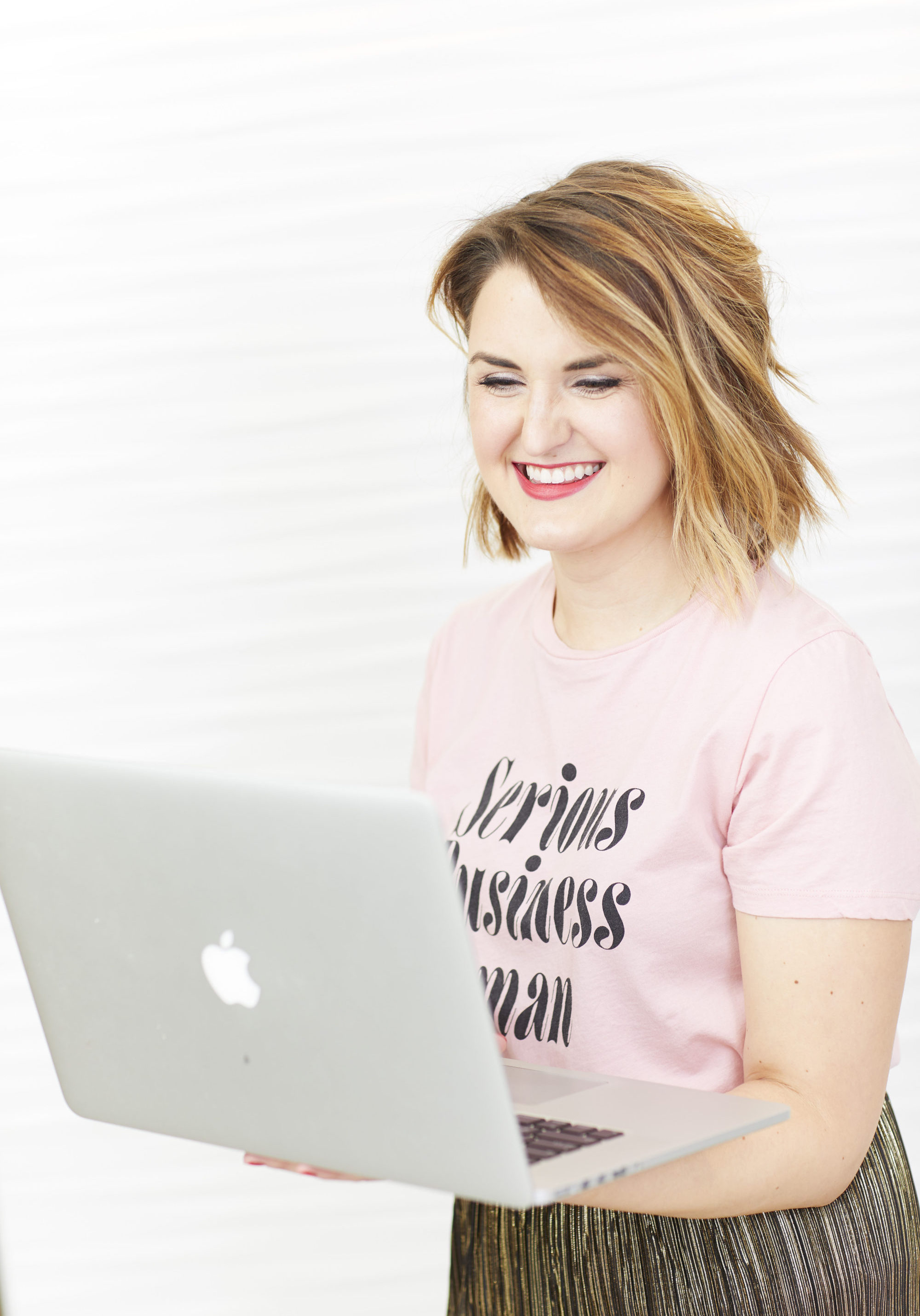 Woman against a white backdrop, smiling and holding a mac laptop